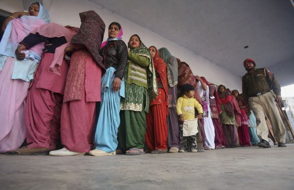Voters wait in a queue to cast their ballots as a policeman walks past outside a polling station at Banur, on Monday
