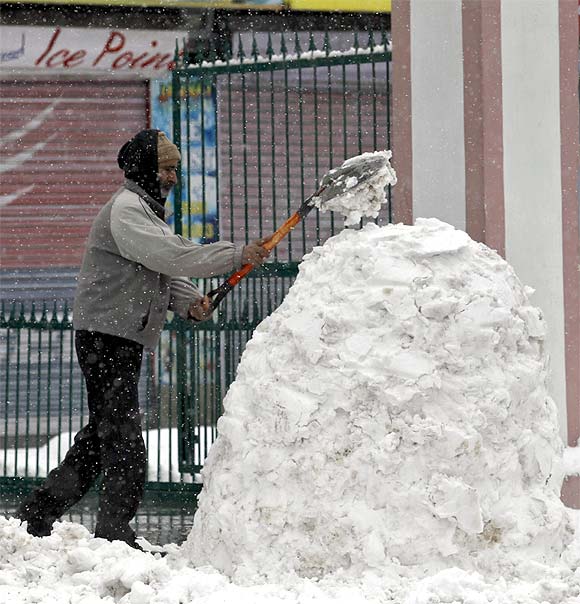 A man shovels snow into a heap outside his shop during snowfall in Srinagar