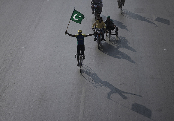 A supporter of the Pakistan People's Party holds the country's national flag while cycling during an anti-US rally