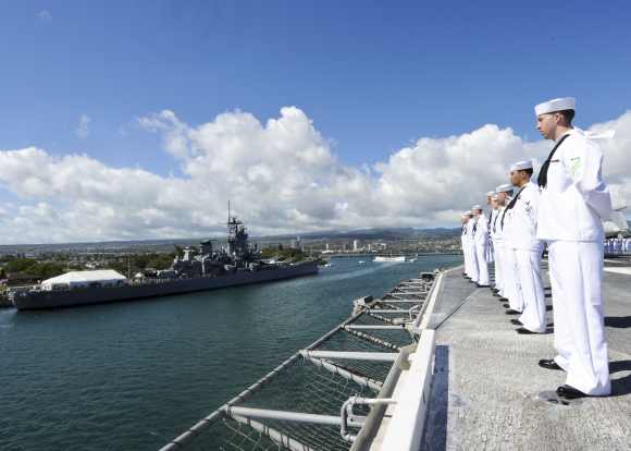 Sailors stand at parade rest as the aircraft carrier USS Nimitz passes the USS Missouri Battleship Memorial and the USS Arizona Memorial in Pearl Harbor