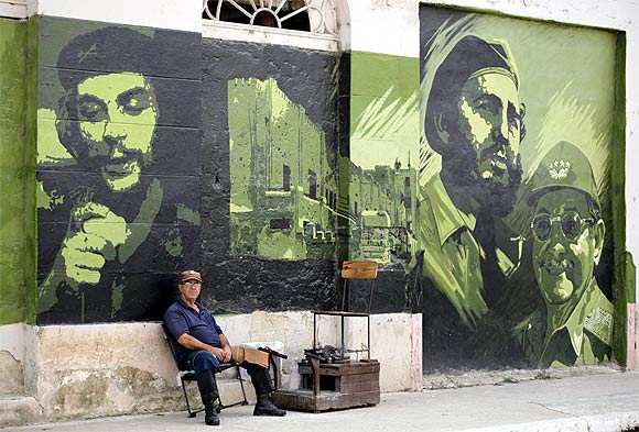 A man waits for customers at his shoe-cleaning stall beside a mural with images of revolution leader Che Guevara, former Cuban leader Fidel Castro and current President Raul Castro in Sagua La Grande, around 240 km east of Havana