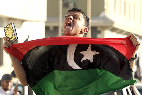 -A man carries a Koran and a Kingdom of Libya flag during a demonstration in Benghazi June 7, 2012  to demand the application of Islamic law, or Sharia law, in Libya