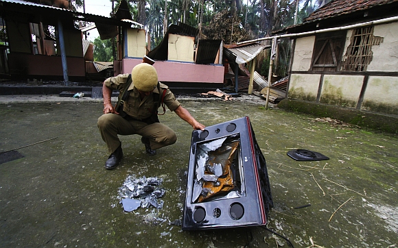 A policeman inspects a damaged television set in the forecourt of a burnt house during violence near Goshaigaon town in Assam