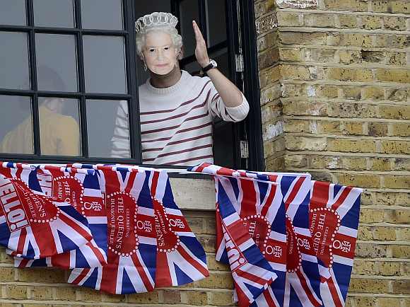 A man wearing a mask of Britain's Queen Elizabeth waves while watching a pageant in celebration of the Queen's Diamond Jubilee in central London