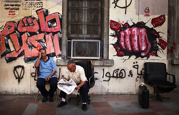 An Egyptian man reads a newspaper in front of a mural in Tahrir square in Cairo