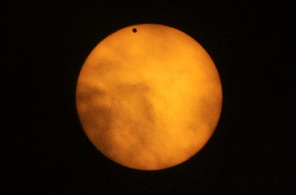 Planet Venus, pictured as a black dot, is seen in transit across the sun during a break in cloud cover at sun in Guwahati