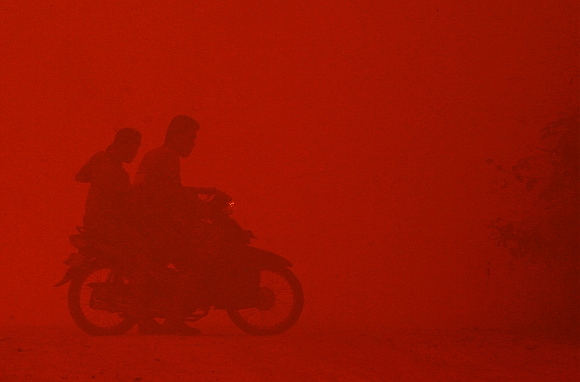 A motorcyclist turns back due to intense heat while passing through haze near burnt peat land in Rokan Hilir, Indonesia's Riau province