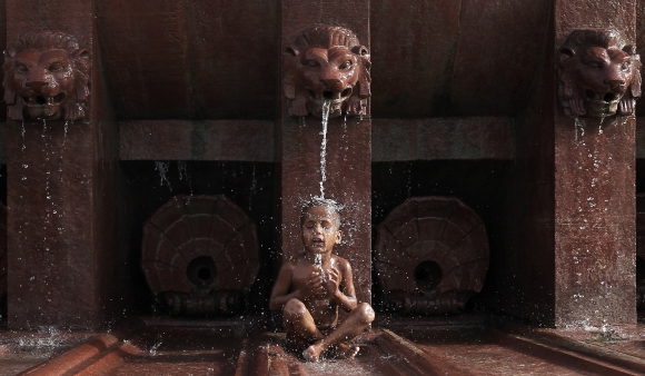 A boy sits under a fountain