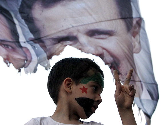 A child with the Syrian opposition flag painted on his face shows the victory sign in front of a burnt picture of Syrian President Bashar al-Assad during a demonstration against the Syrian and Russian governments