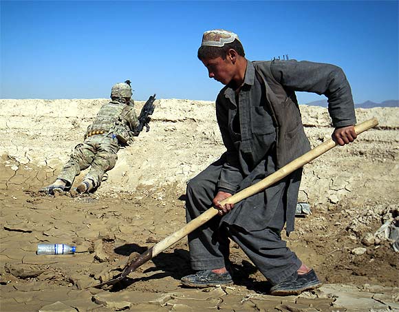 An Afghan boy works at a construction site as a U.S. Army soldier of 3/1 AD Task Force Bulldog takes position during a joint patrol with Afghan National Army (ANA) in a village in Kherwar district in Logar province, eastern Afghanistan
