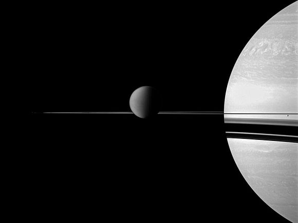 The Cassini spacecraft views Saturn with a selection of its moons in varying sizes. Titan is in the center of the image, while smaller moon Enceladus is on the far right.