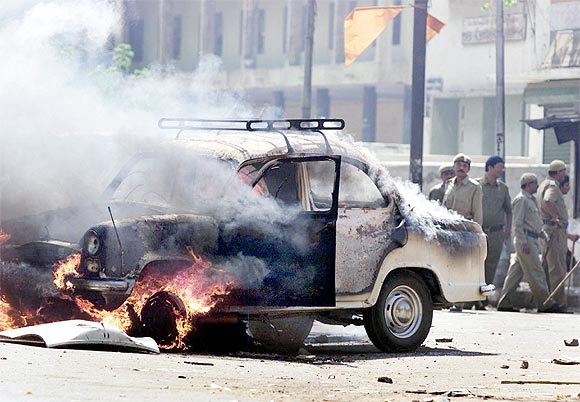 Policemen watch a car set ablaze by rioters in the street in Ahmedabad, during the 2002 riots