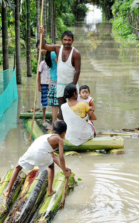 A family wades through flood waters on a boat made out of a banana tree