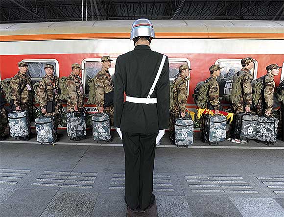A soldier stands guard as recruits walk in a line before boarding a train at the railway station in Nanjing, Jiangsu province, China