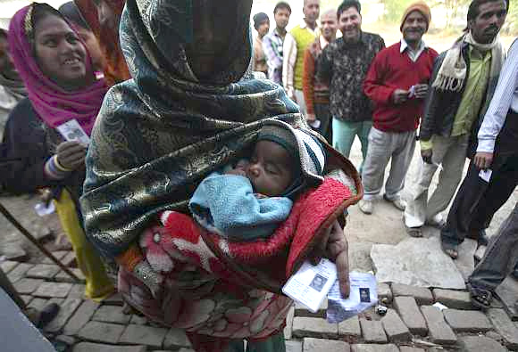 A woman holds her baby and her voter identity card as she waits for her turn to cast her ballot at a polling station