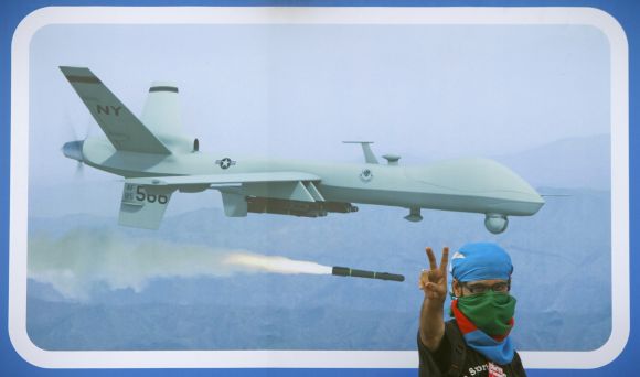 A supporter of Jamaat-e-Islami flashes victory sign in front of a poster of US drone to protest against the alleged killing of Ilyas Kashmiri