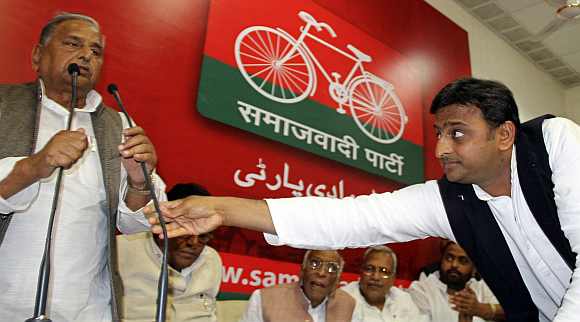 Akhilesh Yadav adjusts the microphone for his father Mulayam Singh during a meeting with newly-elected legislators
