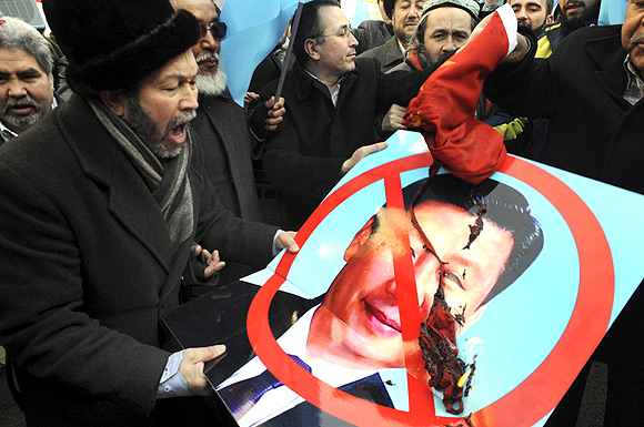 Ethnic Uighur demonstrators hold a defaced poster of China's Vice-President Xi Jinping