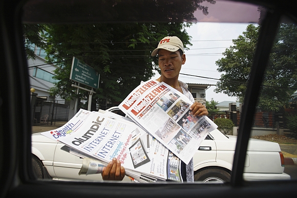 A street vendor selling weekly journals displays some journals towards a vehicle stopping at a red light in Yangon.