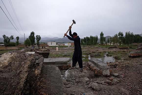 A boy uses a hammer to break a concrete block to scavenge for iron from the demolished compound in Abbottabad