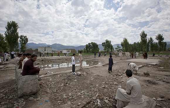 Residents sit near children playing cricket on the demolished site of a compound of Osama bin Laden