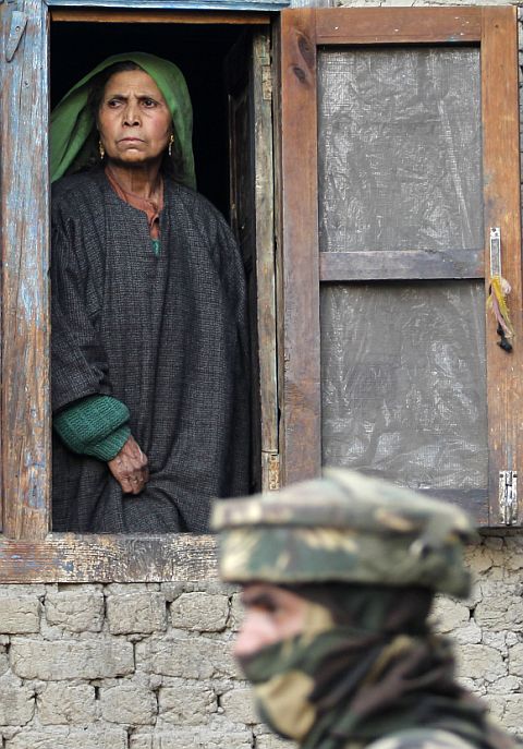 A Kashmiri woman looks out from the window of her house as an Indian soldier keeps guard during a gun battle between security forces and terrorists in the village of Dadsar, 37 km south of Srinagar