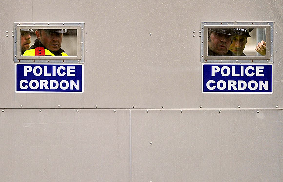 Police officers look through apertures in a mobile steel cordon at the entrance to Whitehall, during a protest march, in central London