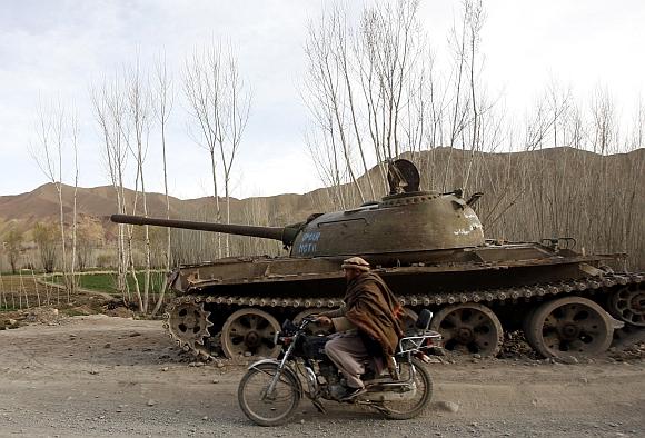 An Afghan man rides a motorcycle past the rusting remains of a Russian tank in Bamiyan province