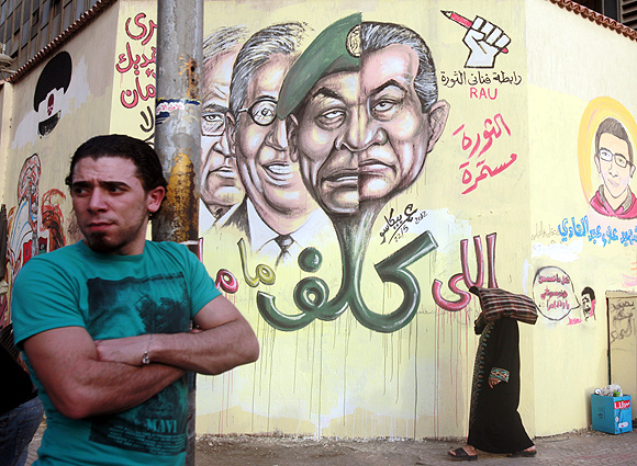 A man stands next to graffiti depicting former President Hosni Mubarak and several presidential candidates, at Tahrir square in Cairo