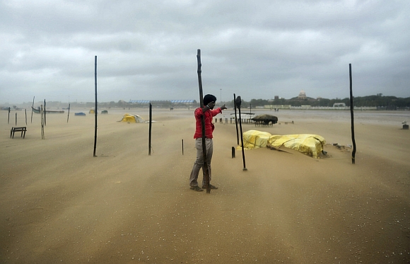 A man holds onto a wooden stick during strong winds at Marina beach in Chennai