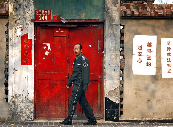 A security guard walks past eviction notices stuck to the exterior wall of a house before it is demolished in central Beijing