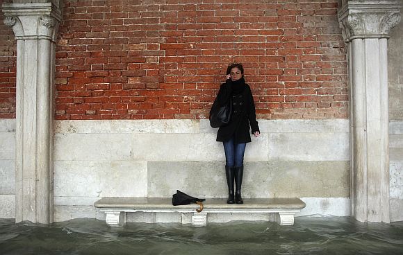 A woman stands on a bench above a flooded street during a period of seasonal high water in Venice