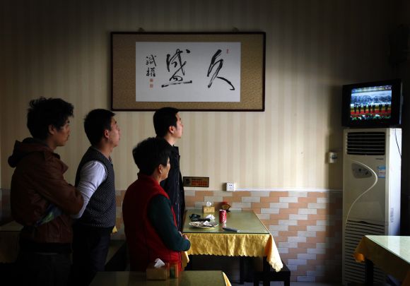 A customer stands with restaurant workers underneath a painting of Chinese characters that reads Long-lasting Prosperity, as they watch television showing the new leadership line-up of China's ruling Communist Party at the Great Hall of the People in Beijing