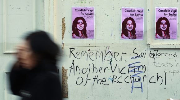 A woman walks past posters advertising a candlelit vigil at the University Hospital Galway in Galway, Ireland