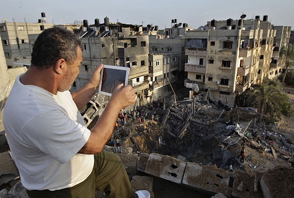 A Palestinian man uses his iPad as he takes pictures of a destroyed house after an Israeli air strike in Khan Younis in the southern Gaza Strip