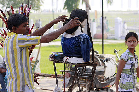 A seller of wigs displays different hairstyles near the ghat