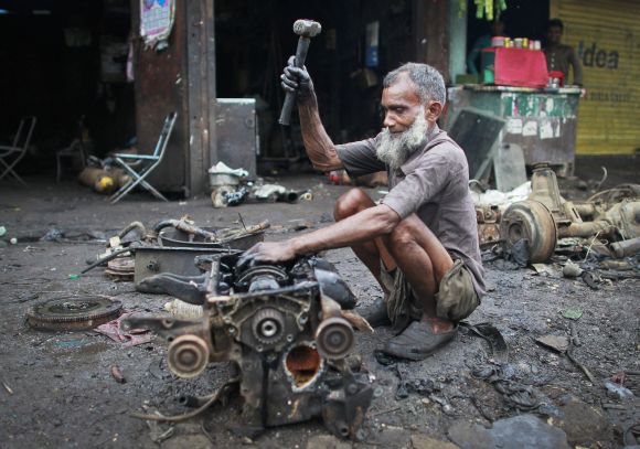 Hamid, uses a hammer to break an engine outside a scrapyard at an industrial area in Mumbai