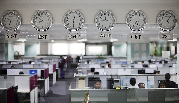 Workers pictured beneath clocks displaying time zones at an outsourcing centre in Bengaluru