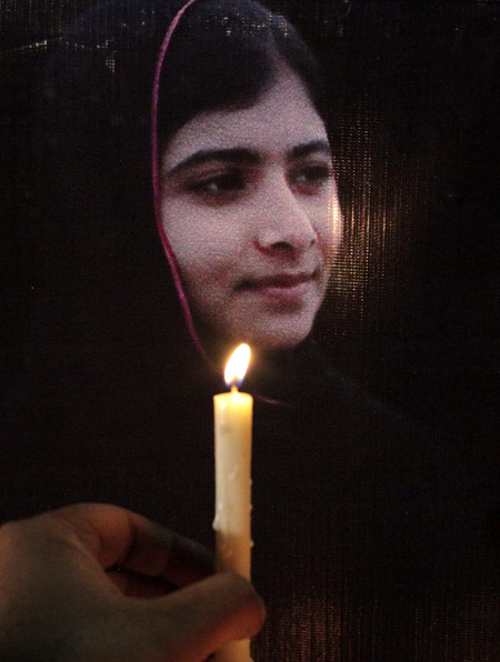 A man holds a candle next a picture of Malala Yousufzai, who was shot by the Taliban for speaking out against the militants and promoting education for girls, at a school in Lahore