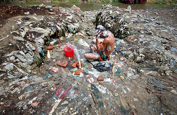 A man bathes from a broken water pipe line in a Noida slum in Uttar Pradesh
