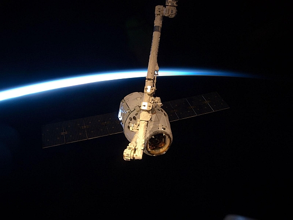 With darkness, earth's horizon and thin line of atmosphere forming a backdrop, the SpaceX Dragon commercial cargo craft is grappled by the Canadarm2 robotic arm at the International Space Station