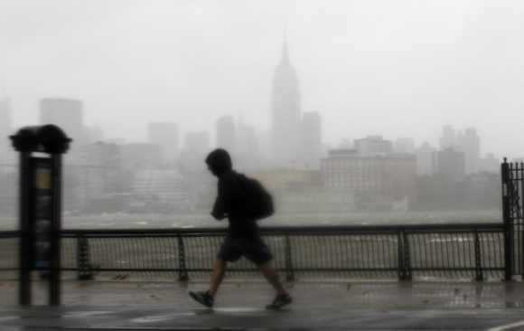 A man walks into the wind across the Hudson River from the skyline of New York in Hoboken
