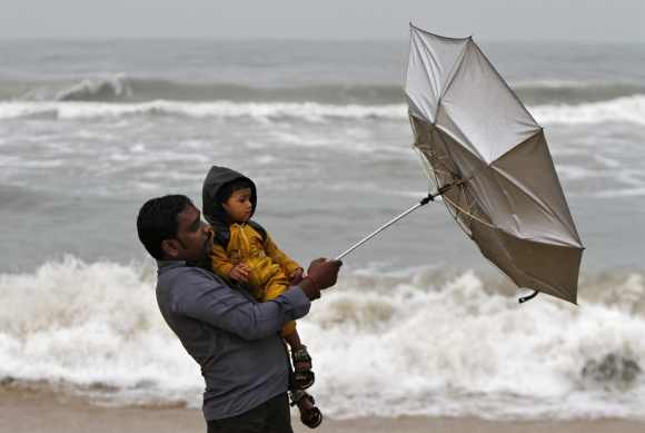 A man carrying his child tries to hold an umbrella at Marina beach in Chennai