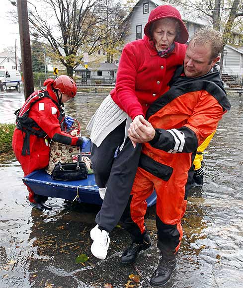 An emergency personnel lifts an elderly resident out of a rescue boat to dry land away from flood waters brought on by Hurricane Sandy in Little Ferry, New Jersey