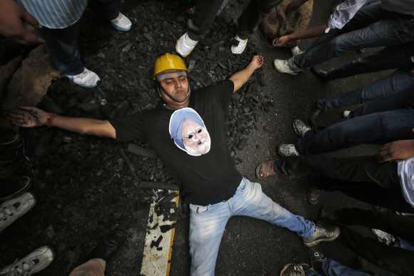 An activist from Bharatiya Janata Yuva Morcha, wearing a cut-out of India's Prime Minister Manmohan Singh, lies on a heap of charcoal during a protest in New Delhi