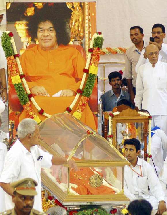 Devotees sit beside the body of spiritual guru Sri Sathya Sai Baba at an ashram at Puttaparti, Andhra Pradesh on April 24, 2011