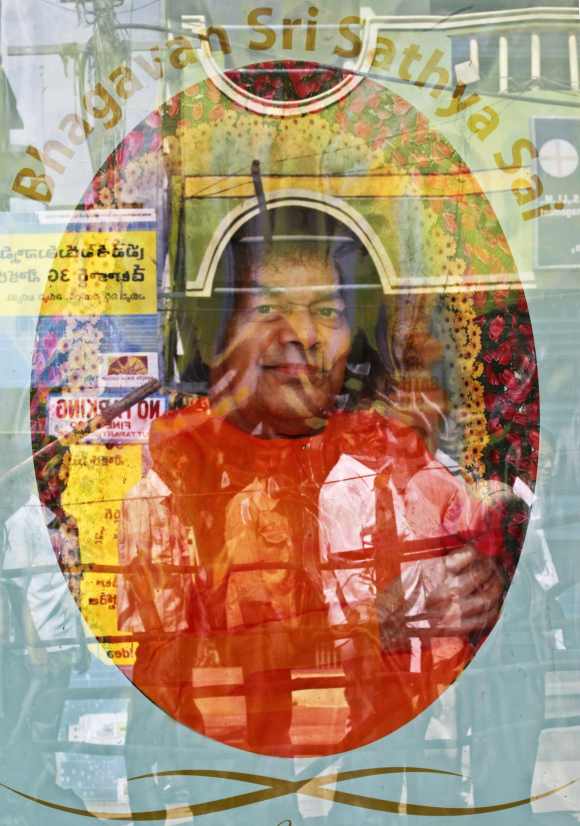 Devotees are reflected in a the window of a shop displaying a photograph of spiritual guru Sri Sathya Sai Baba