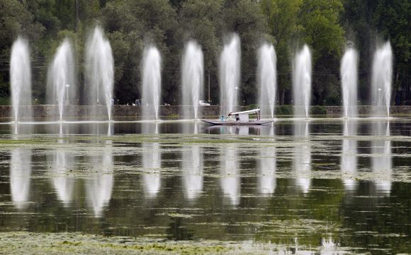 A Kashmiri man rows a boat past fountains in the polluted waters of Dal Lake, in Srinagar