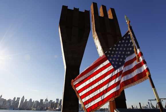 A US flag flies at a memorial bearing two pieces of steel from the World Trade Center in Weehawken, New Jersey, across from the skyline of New York