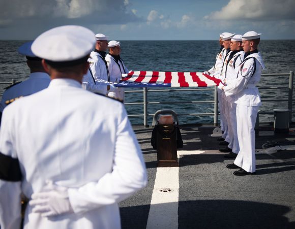 Members of the US Navy ceremonial guard hold an American flag over the remains of Neil Armstrong in the Atlantic Ocean